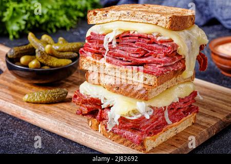 Nahaufnahme des reuben-Sandwiches mit Roggenbrot, dünn geschnittenem Corned Beef, Sauerkraut, russischem Dressing und geschmolzenem Käse an Bord mit Gurken Stockfoto