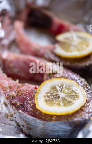 Rohe Silberkarpfen-Steaks mit Zitrone. Mit Gewürzen bestreut liegen auf der Folie. Vorbereitung zum Kochen. Stockfoto