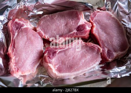 Rohe Fleischsteaks auf Folie. Schweinefleisch. Vorbereitung für das Kochen im Ofen. Stockfoto