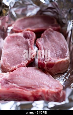 Rohe Fleischsteaks auf Folie. Schweinefleisch. Vorbereitung für das Kochen im Ofen. Stockfoto