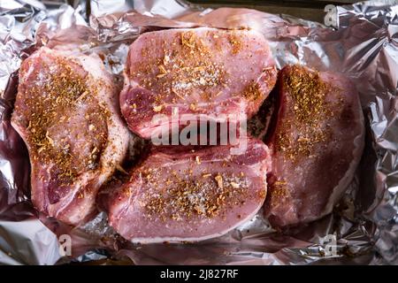 Rohe Fleischsteaks auf Folie. Schweinefleisch mit Gewürzen bestreut. Kochen ohne Öl. Vorbereitung für das Kochen im Ofen. Stockfoto