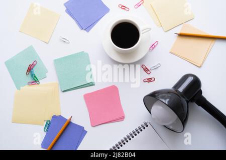 Draufsicht auf eine Tasse Kaffee in der Nähe von Schreibwaren und Lampe auf Weiß Stockfoto