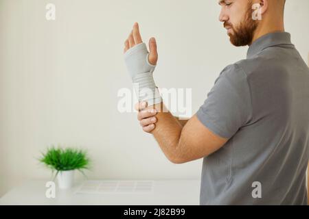 Der Mann mit Sehnenentzündung oder Karpaltunnelsyndrom trägt zur Kompression und Schmerzlinderung eine Handgelenkstütze Stockfoto