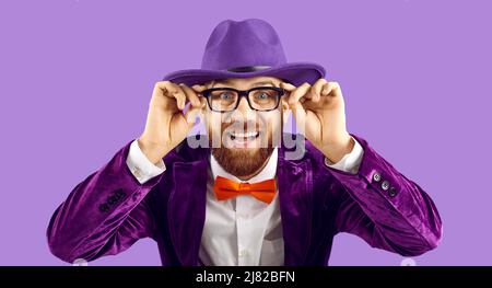 Porträt von lustigen fröhlichen stilvollen Showman, der Brille trägt, während auf lila Hintergrund. Stockfoto