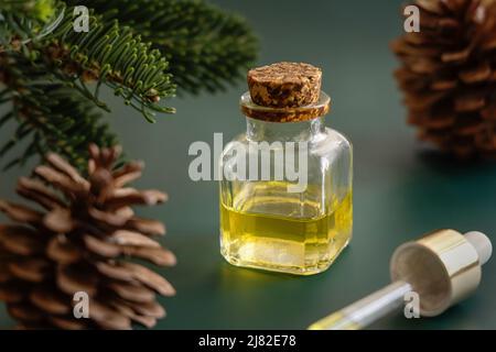 Glasflasche und Tropf mit ätherischem Nadelöl in der Nähe von Tannenzweigen und Tannenzapfen auf grünem Nahaufnahme. Aromatherapie, Spa und Kräutermedizin Konzept. Stockfoto