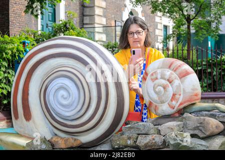 London, Großbritannien, 12.. Mai 2022. Catherine Boardman, Bloggerin von „Cultural Wednesdays“, schaut sich die neue Installation an und fotografiert. Sculpture in the City startet seine erste öffentliche Kunstkommission „Earthing“ für die Aldgate Square Commission von Jocelyn McGregor am Aldgate Square in der City of London. Jocelyn spielt mit Taktilität und hat eine Kombination von Materialien wie Acryl, Jemonit, Stein und Bronze gemischt. Sie ist darauf bedacht, dass ihre Arbeit berührt wird, und wurde absichtlich nicht auf einen Sockel gestellt, was darauf hinweist, dass jedes Material eine andere Porosität, Temperatur und Haptik hat. Das A Stockfoto