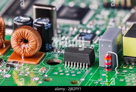 Spule oder verschiedene elektronische Komponenten auf grüner Leiterplatte. Orangefarbene Induktivität mit Kupferdraht, schwarzem ethernet-Trenntransformator und Diode. Stockfoto