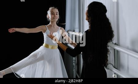 Kaukasisches Mädchen Teenager Student Ballerina in Tutu tun Tanzübungen in der Nähe von Ballett Barre hören Erklärungen Ratschläge von erwachsenen Lehrerin weiblich Stockfoto