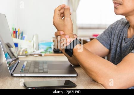 Der Mann fühlte sein Handgelenk verletzt, während er zu Hause mit einem Laptop unterwegs war. Stockfoto