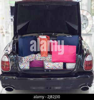 Der offene Kofferraum des Autos ist mit Einkaufstaschen aus dem Einkaufszentrum gefüllt. Weihnachtseinkäufe. Stockfoto