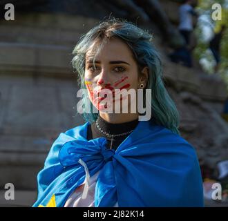 Porträt einer Aktivistin mit ukrainischer Nationalflagge und einer blutigen Hand auf dem Gesicht Stockfoto