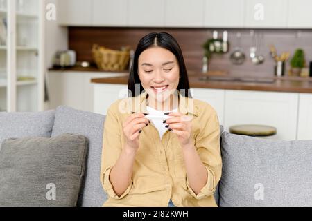 Zufriedene glückliche junge Frau sitzt auf der Couch zu Hause mit Schwangerschaftstest und feiert Ergebnis, freut sich auf erwartete Mutterschaft Stockfoto