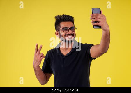 Lächelnder, hübscher inder, der Selfie auf gelbem Hintergrund fotografiert Stockfoto