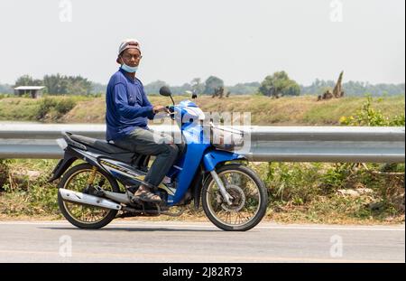 SAMUT PRAKAN, THAILAND, APR 14 2022, Ein Mann mit Gesichtsmaske fährt ein Motorrad auf der Landstraße Stockfoto