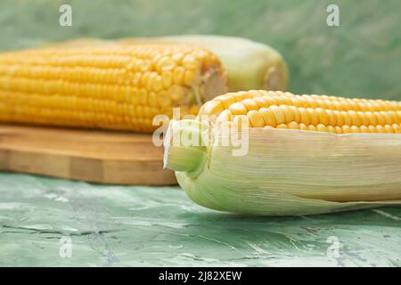 Gelbe rohe Maiskolben auf Holzbrett auf dem Tisch. Aquarell grüner Hintergrund. Essen, Vegetarismus. Speicherplatz kopieren Stockfoto