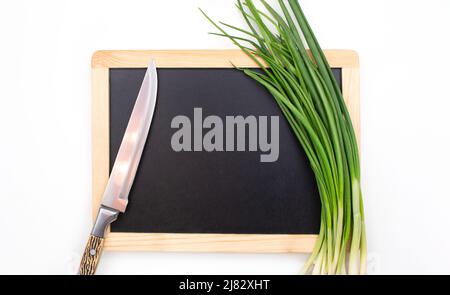 Grüne Zwiebel und Messer auf Schneidebrett auf isoliertem Hintergrund. Zutat, Zubereitung. Speicherplatz kopieren Stockfoto