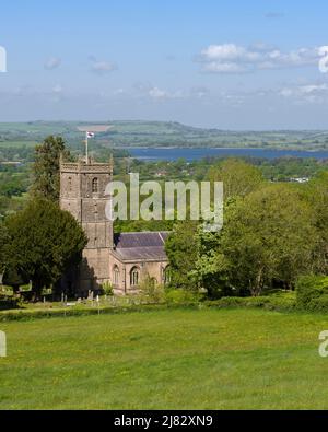 Die Kirche St. Michael des Erzengels im Dorf Compton Martin am Fuße der Mendip Hills mit dem Chew Valley Lake Reservoir im Jenseits, Somerset, England. Stockfoto