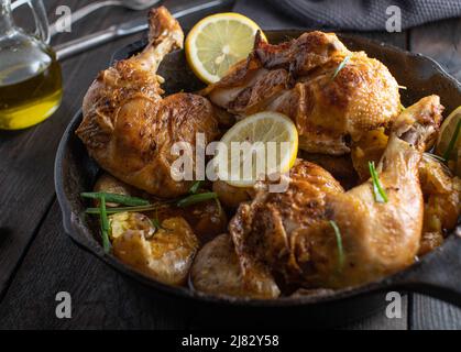 Geschmorte Hähnchenschenkel mit Sauce und Kartoffeln in einer gusseisernen Pfanne auf einem Holztisch. Mediterranes Fleischgericht Stockfoto