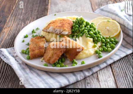 Panierter Rotbarsch mit Kartoffelpüree und grünen Erbsen auf einem Teller Stockfoto