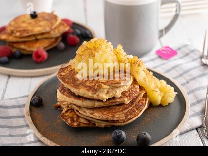 Gesunde Proteinpfannkuchen zum Frühstück, die aus Eiern, Quark und Hafer hergestellt werden. Serviert mit hausgemachter Apfelsauce auf einem Teller Stockfoto