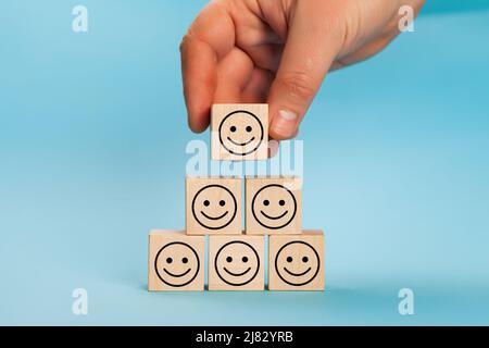 Bewertung der Kundenerfahrung. Hand Putting Holzwürfel Blockform mit Symbol Gesicht Smiley, die beste ausgezeichnete Business-Services Bewertung Kunden Stockfoto