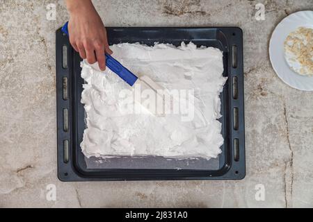 Der Konditor streut die Baiser eines kulinarischen Silikonspatels auf ein Backblech zum Backen im Ofen Stockfoto