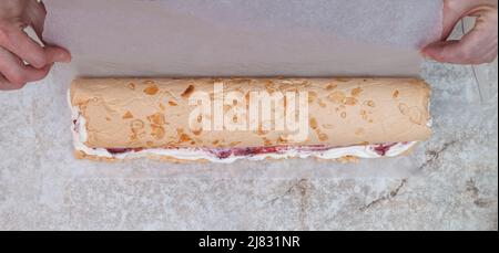 Der Konditor des Küchenchefs rollt die Baiser zu einer Rolle mit Beerenconfit und Creme Stockfoto