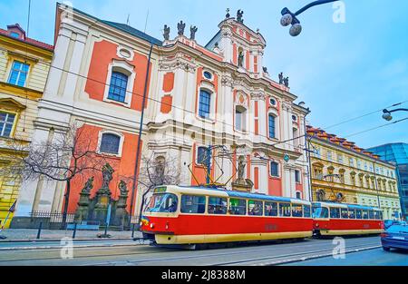 Die leuchtend rote Vintage-Straßenbahn, die die Narodni-Allee vor der St. Ursula-Kirche in Prag, Tschechische Republik, hinunterfährt Stockfoto