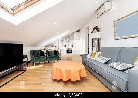 Dachwohnung mit offener Küche und Wohnzimmer, blauem Stoff faltbares Dreisitzer-Schlafsofa, TV auf schwarzem Tisch und Vintage-Beistelltisch Stockfoto
