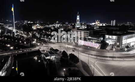 Beleuchteter Flussdamm mit Flagge der Ukraine und Nachtsicht. Stadt Luftpanorama über dem Fluss Lopan in der Nähe der Dormition Kathedrale in Kha Stockfoto