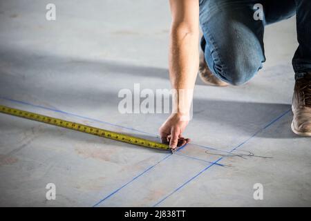 Bauarbeiter, der den Boden misst, als Teil der Umrissen für die Installation von Metallrahmen. Stockfoto