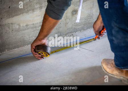 Bauarbeiter, der den Boden misst, als Teil der Umrissen für die Installation von Metallrahmen. Stockfoto