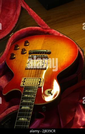Foto von vintage Les Paul Gitarrenkörper, zeigt Abnutzung von Lack. Die Gitarre ist auf einem gegerbten Etui mit rosafarbenem Filzinterieur platziert. Stockfoto