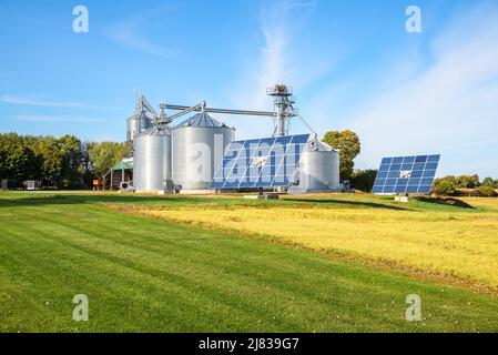 Sonnenkollektoren mit Getreideaufzug mit großen Stahllagerbehältern im Hintergrund in einem modernen Bauernhof an einem sonnigen Herbsttag Stockfoto