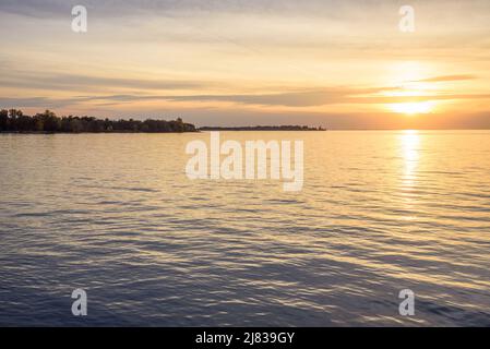 Schöner Herbstuntergang über einem See. Eine Insel mit Windturbinen, die am Horizont sichtbar sind. Ruhige Szene. Lake Ontario, Kanada. Stockfoto