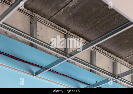 Installiert unteren verzinkten Stahl quadratische Fliese Drop-Down-Decke mit lackiertem Trockenbau, aussetzen Metallrahmen hinter dem Trockenbau. Dies ist eine Schulklasse. Stockfoto