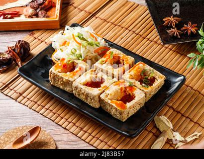 Knusprig gebratener Stinky Tofu in einem schwarzen Tablett mit rotem Chili isoliert auf matter Seitenansicht japanischer Speisen Stockfoto