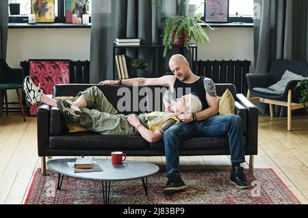Tätowierte ältere kaukasische Mann und Frau in der Liebe tragen lässige Kleidung zusammen entspannen auf der Couch im Loft Wohnzimmer zu Hause Stockfoto