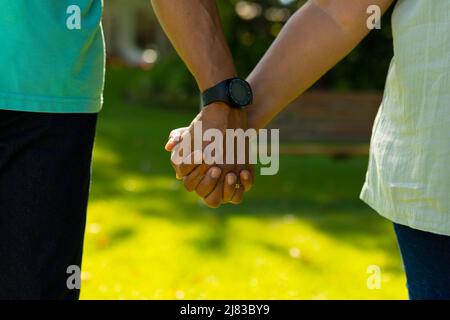 Mittelteil eines älteren Birazialmannes, der eine Armbanduhr mit der Hand der Frau trägt, während er im Park steht Stockfoto