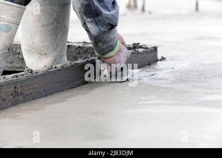 Bauarbeiten mit seinem Stahlkanter, um die Ecken einer frisch gegossenen Betonplatte eines Wohngebäudes zu glätten. Stockfoto