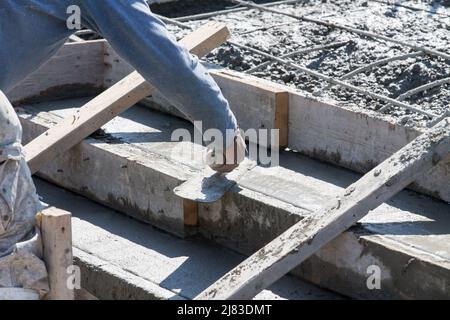 Der Bauarbeiter verwendet eine Fertigkelle, um frisch gegossene Betonstufen oder Treppen auf einem neuen Wohngebäude zu glätten. Stockfoto