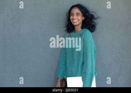 Glückliche schöne junge biracial Geschäftsfrau mit Tablet-pc steht gegen graue Wand am Arbeitsplatz Stockfoto
