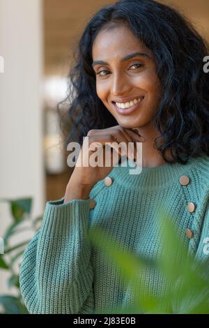 Lächelnde junge biracial Geschäftsfrau mit Hand auf Kinn am Arbeitsplatz Stockfoto