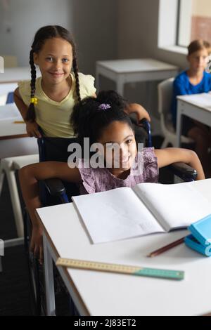 Porträt eines kaukasischen Elementarmädchen, das neben einer biracial Mitschülerin auf dem Rollstuhl sitzt Stockfoto