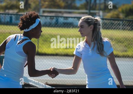 Selbstbewusste junge, multirassische Tennisspielerinnen, die am sonnigen Tag Handschlag auf dem Platz machten Stockfoto