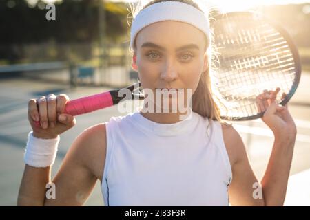 Porträt einer selbstbewussten jungen schönen kaukasischen Spielerin mit Tennisschläger um den Hals Stockfoto