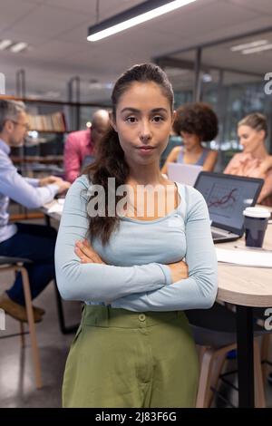 Porträt eines selbstbewussten jungen hispanischen Geschäftsmannes mit gekreuzten Armen gegen biracial Kollegen Stockfoto
