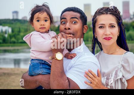 Transnationale interrassische Mutter und Vater, die mit ihrem gemischten Mädchen im Herbstpark spazieren gehen Stockfoto