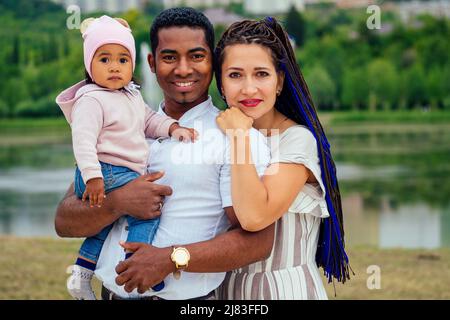 Transnationale interrassische Mutter und Vater, die mit ihrem gemischten Mädchen im Herbstpark spazieren gehen Stockfoto