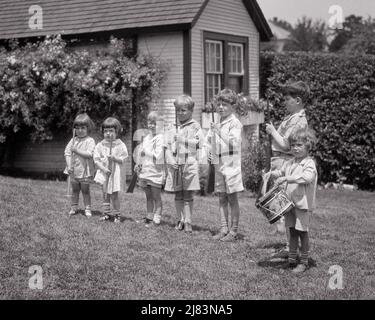 1920S GRUPPE VON JUNGEN UND MÄDCHEN IM HINTERHOF, DIE MIT SPIELZEUGGEWEHREN RECHEN UND STÖCKEN AUF DIE AUFMERKSAMKEIT ALS SOLDATEN SPIELEN UND EIN SCHLAGZEUGER - J735 HAR001 HARS PERSONEN MÄNNER RISKIEREN GESCHWISTER SCHWESTERN B&W ABENTEUER BOHREN UND AUFMERKSAMKEIT SIEBEN FORMATION GESCHWISTER UNIFORMEN 7 DRUMMER FREUNDLICH STICKS STILVOLLE BB PISTOLE SCHUSSWAFFE JUVENILES PRE-TEEN PRE-TEEN JUNGE PRÄSENTIEREN WAFFEN SCHWARZ UND WEISS KAUKASISCH ETHNIZITÄT HAR001 MILIZEN ALTMODISCHE RECHEN Stockfoto